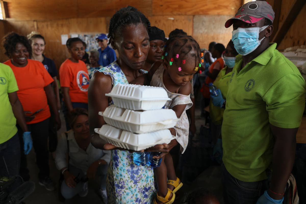 A woman carrying a child walks away with food from the World Food Program (WFP) at the Jean Marie Vincent High School which has been turned into a shelter for families displaced by gang violence in the Tabarre neighbourhood of Port-au-Prince, Haiti, in Jul