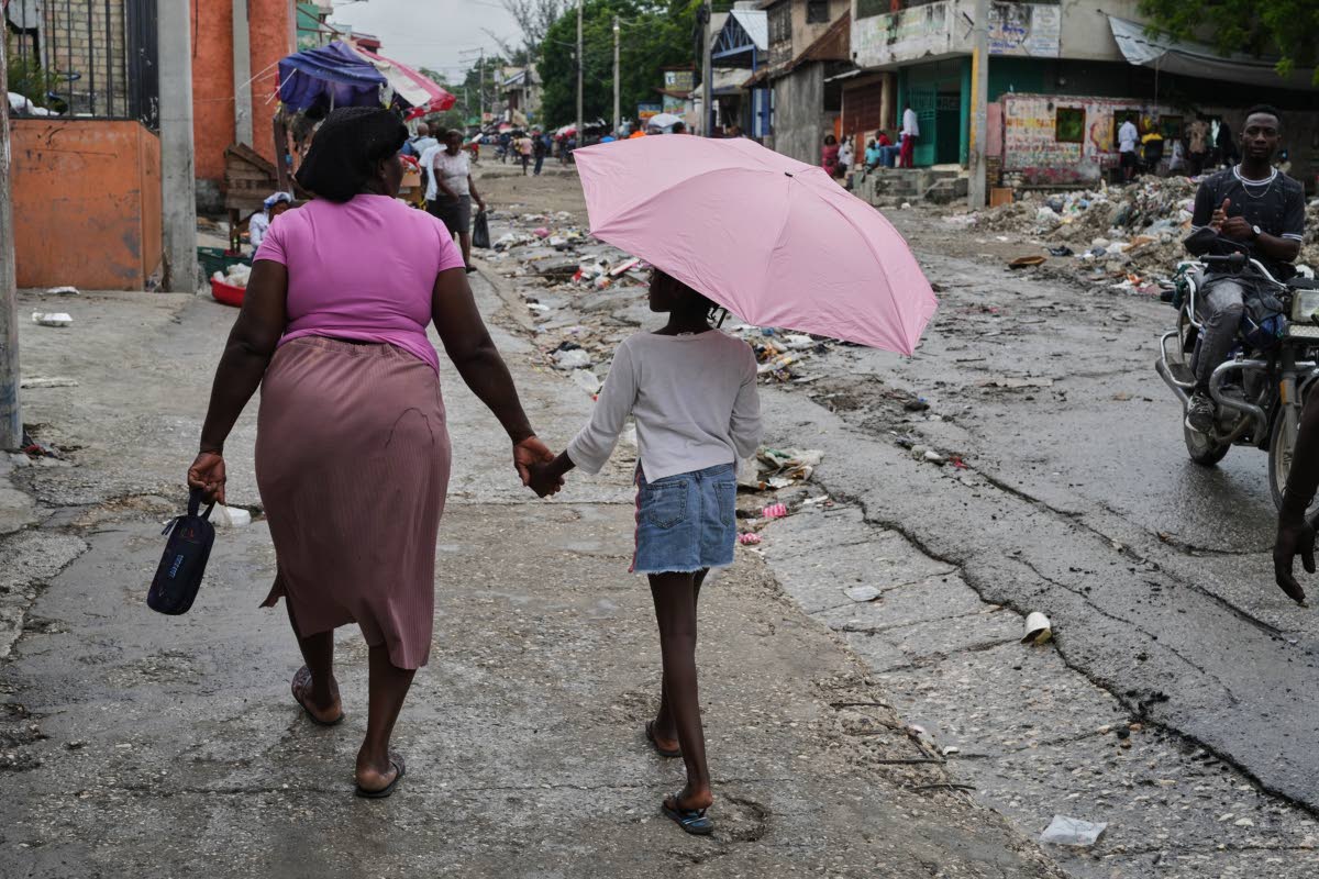 A woman walks hand-in-hand with a small girl during light rain in Port-au-Prince, Haiti.