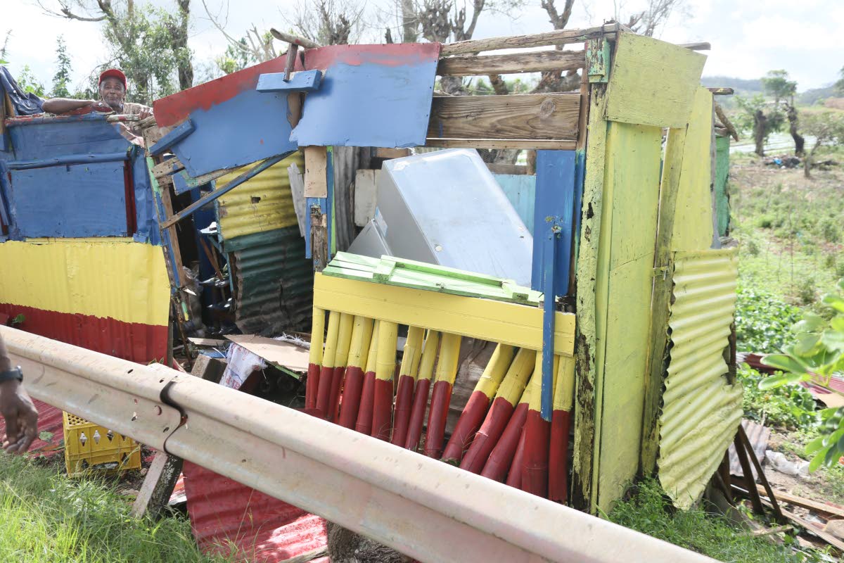 Burnell Morris of Cobbla, Manchester, on Wednesday, uses a tarpaulin to cover his shop along the main road after the structure was damaged during the passage of Hurricane Melissa.