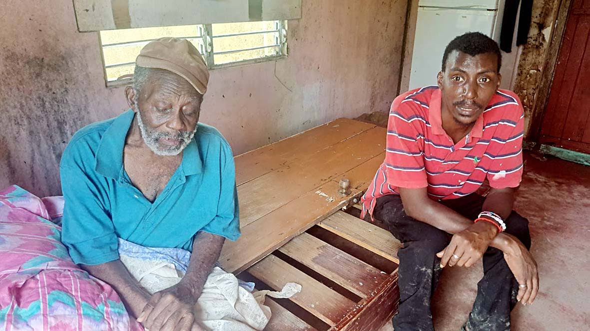 Horace Taylor (left) grieves as caregiver Nigel Wilson (right) recounts the night Hurricane Melissa tore through his home in Adelphi, St. James, killing his wife.