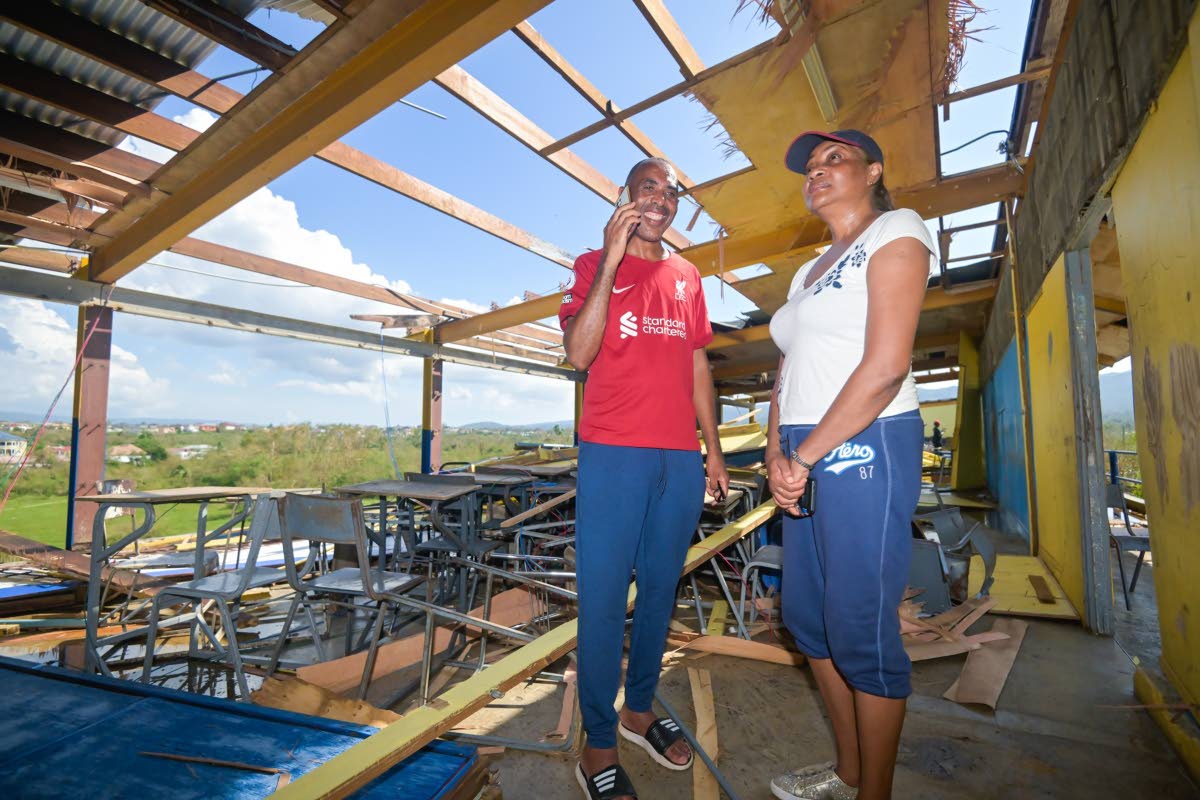 Principal of St Elizabeth Technical High School (STETHS), Keith Wellington, takes calls from persons offering well wishes and support, while the institution’s Acting Vice Principal Patrine Daley-Chambers, looks on the damage to the grade 11 block.  STET