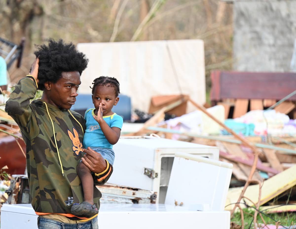 A resident of Shrewsbury, Logwood, in Westmoreland, holds his baby while surveying debris from homes that were battered by the Category 5 Hurricane Melissa as he contemplates his next move.