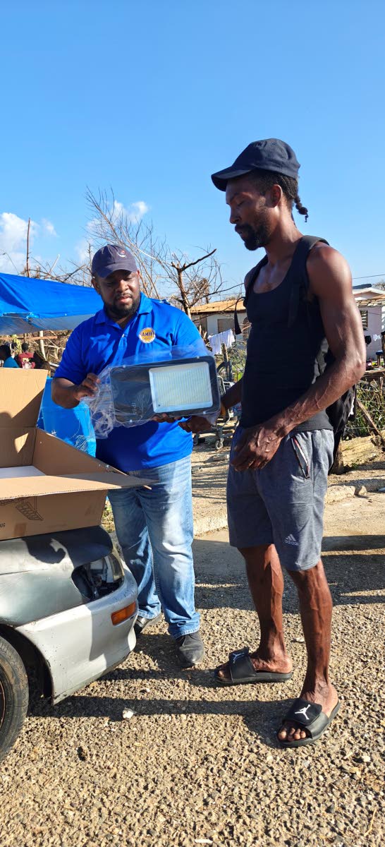 A resident of Logwood watches as Donmayne Gyles, president and CEO of Andrews Memorial Hospital Ltd, unpacks a brand-new solar lantern for him. The gift, courtesy of Nutri Delight, was presented during Andrews Memorial Hospital’s outreach on November 4, 