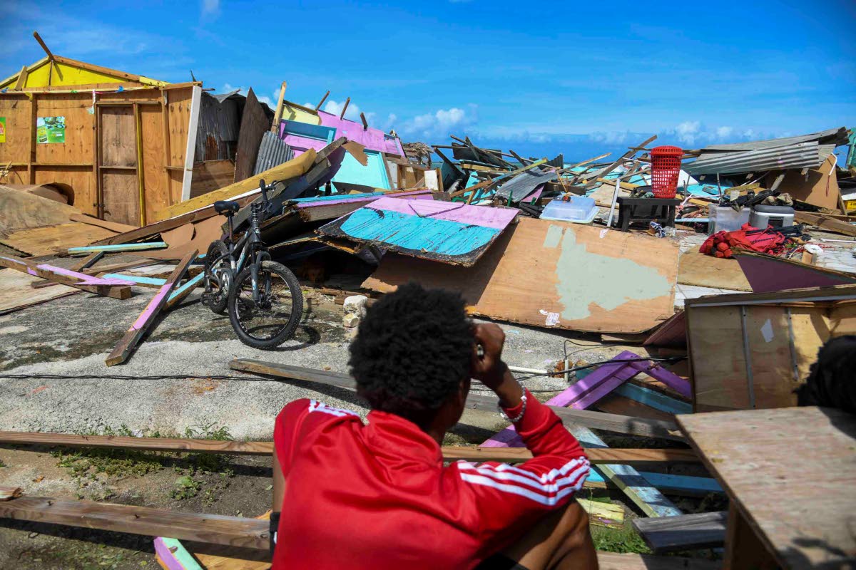 On October 29, a fisherman of Salem in St Ann sits among the rubble holding his head in despair as he looks on at the damage done to the shacks on the Salem fisherman's beach in St Ann.