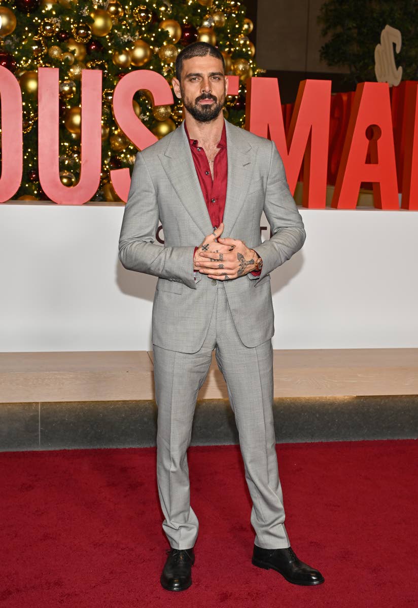 Michele Morrone cuts a sharp figure in a grey suit offset by a deep red shirt.