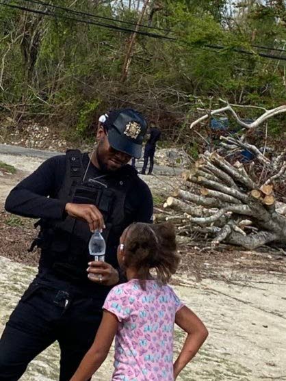 Constable Powell helps an Adelphi Primary School student open a bottle of water amid the devastation at the roofless school during the RG CARES outreach in Adelphi, St James. 