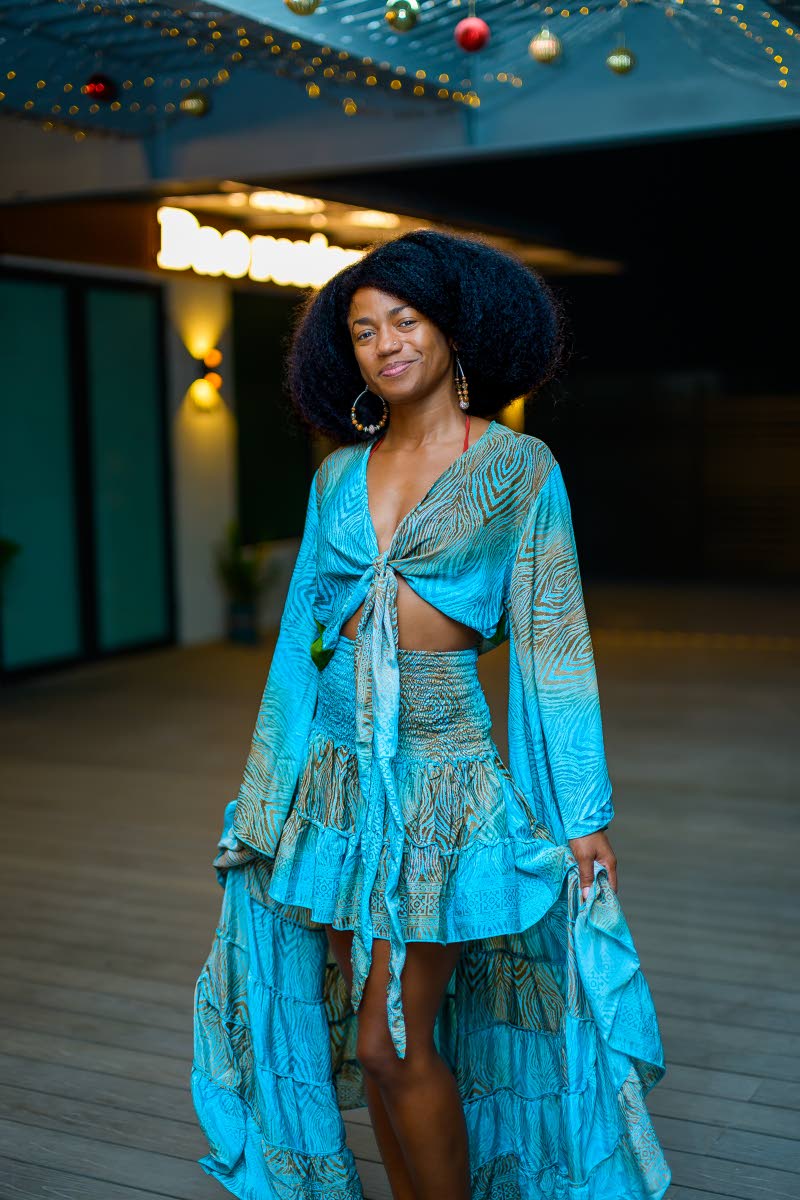 Web Designer, Samiyyah Andrewin-Miranda, stuns in a flowing turquoise outfit featuring a tie-front top with billowy sleeves and a smocked waist, paired with a tiered skirt that adds movement to the look.