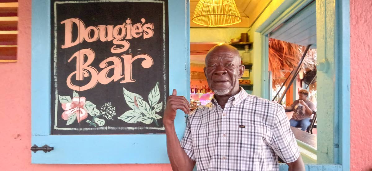 Douglas ‘Dougie’ Turner pointing to the sign of the bar that was named in his honour at Jakes Treasure Beach in St Elizabeth.