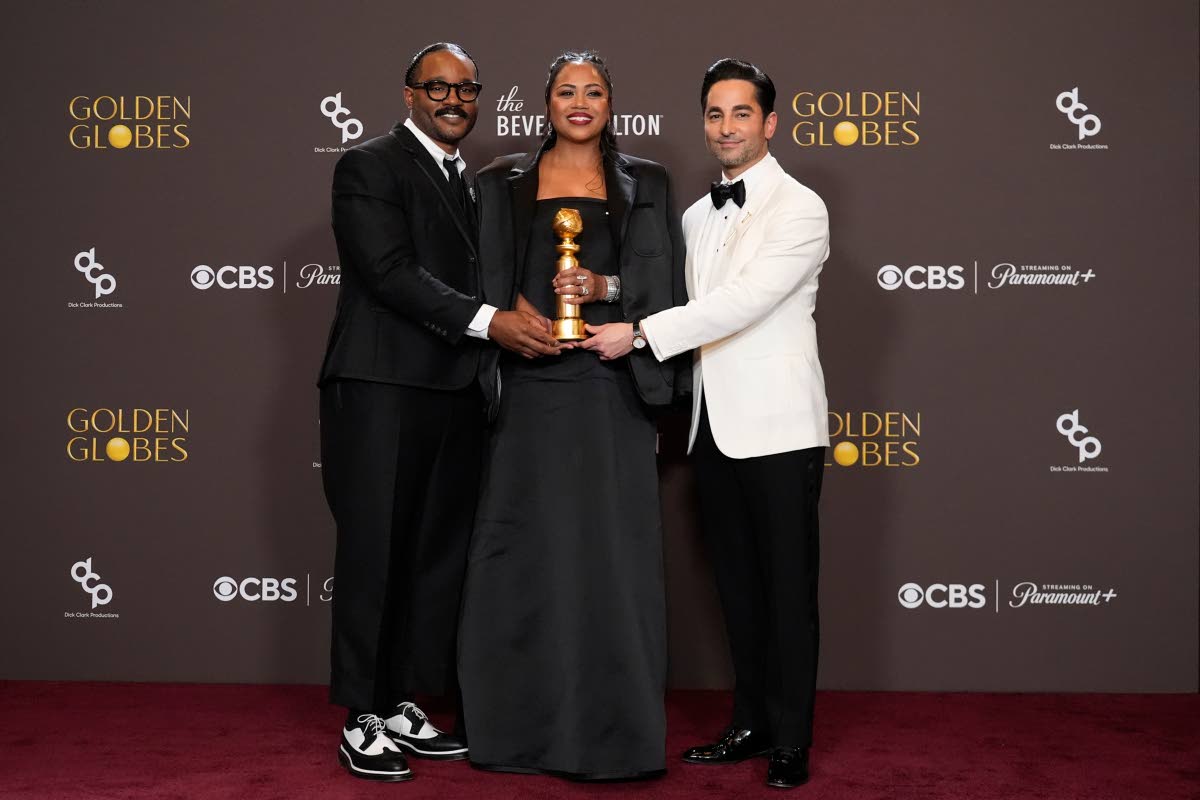 From left: Ryan Coogler, Zinzi Evans, and Sev Ohanian pose in the press room with the award for Cinematic and Box Office Achievement for ‘Sinners’, Coogler and Evans in Thom Browne.