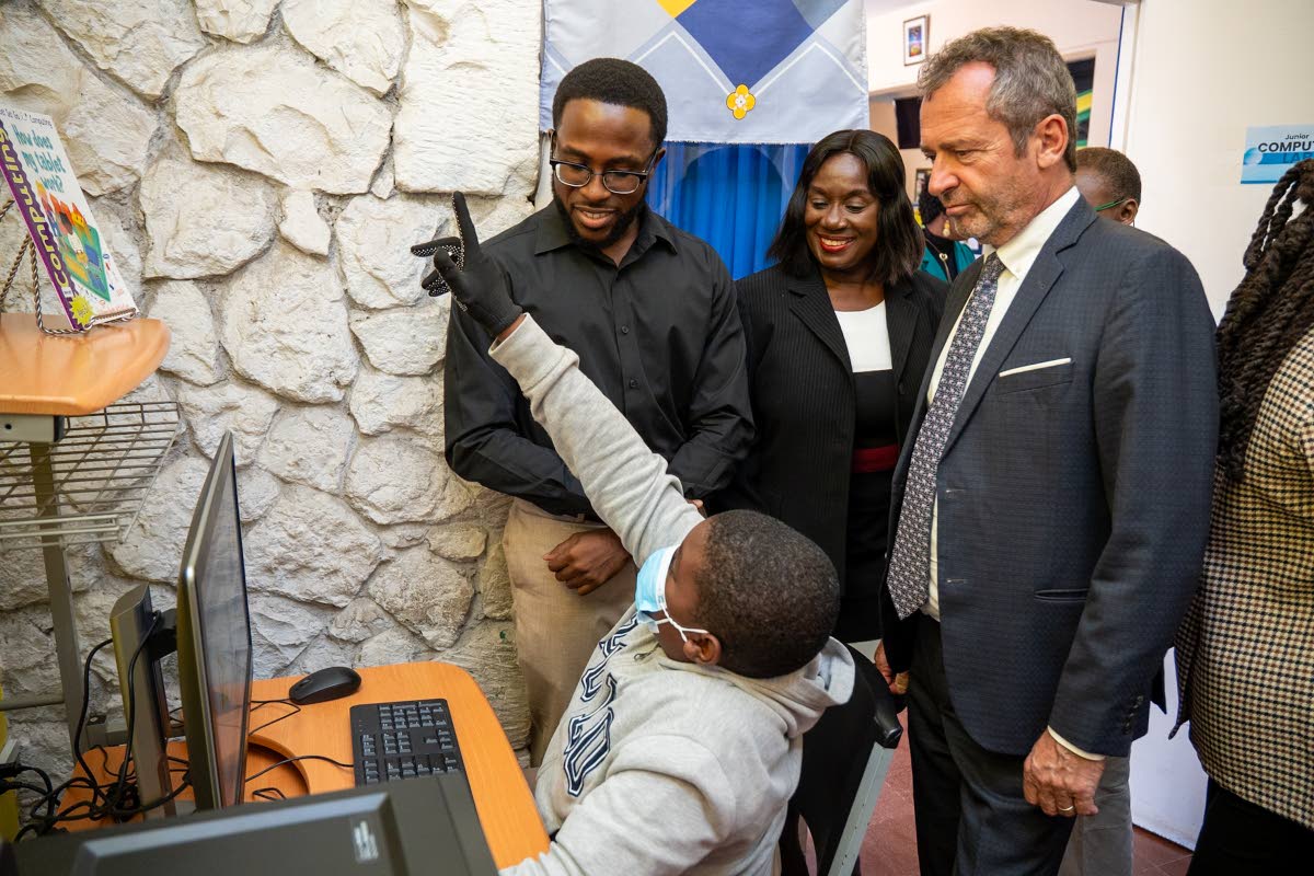 A Chetwood Memorial Primary School student uses a desktop computer as JLS Communications Director Royane Green (standing left), JLS Director General Maureen Thompson (centre), and UNESCO Caribbean Director Eric Falt (right) look on.