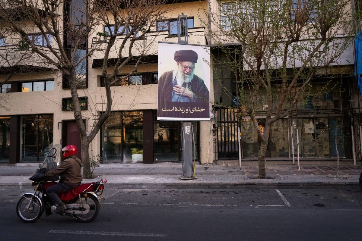 A motorcycle drives past a picture of the late Iranian Supreme Leader Ayatollah Ali Khamenei along an empty street in Tehran, Iran on March 1, 2026, following the confirmed death of Khamenei in US and Israeli strikes. (AP Photo/Vahid Salemi)