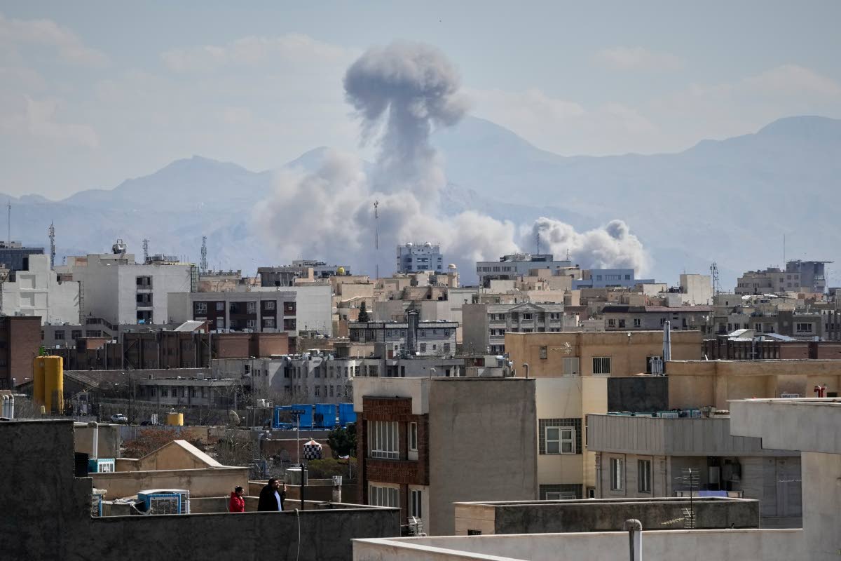 People watches from a rooftop as a plume of smoke rises after a strike in Tehran.