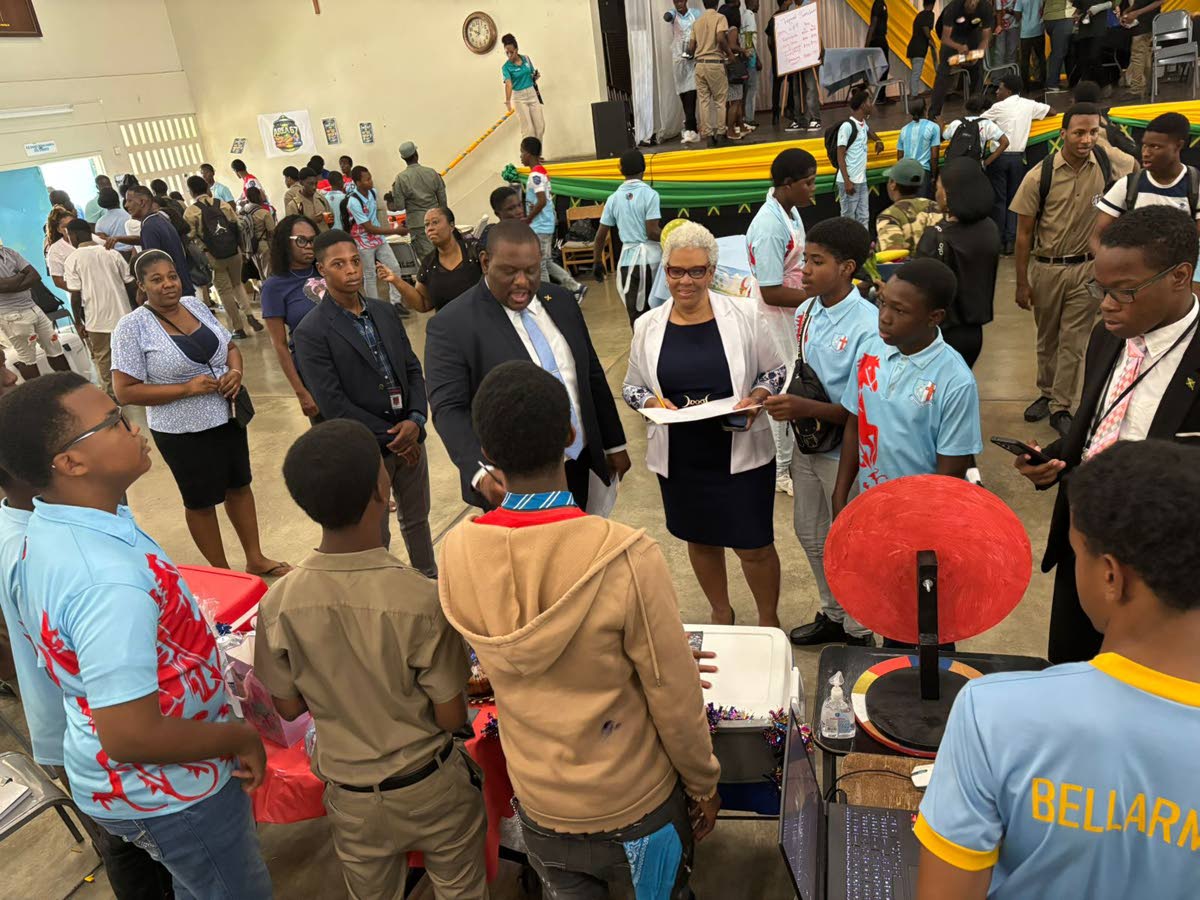 Senator Marlon Morgan, parliamentary secretary in the Ministry of Education, Skills, Youth and Information, engages with a group of students at the STGC Teen Biz Expo 2026 as St George’s College Principal Margaret Campbell looks on.