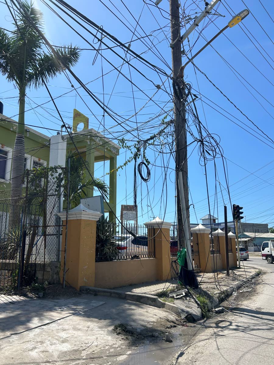Low-hanging cables drape across a sidewalk at Dunbar’s River in Savanna-la-Mar, forcing pedestrians into the busy roadway and raising safety concerns.