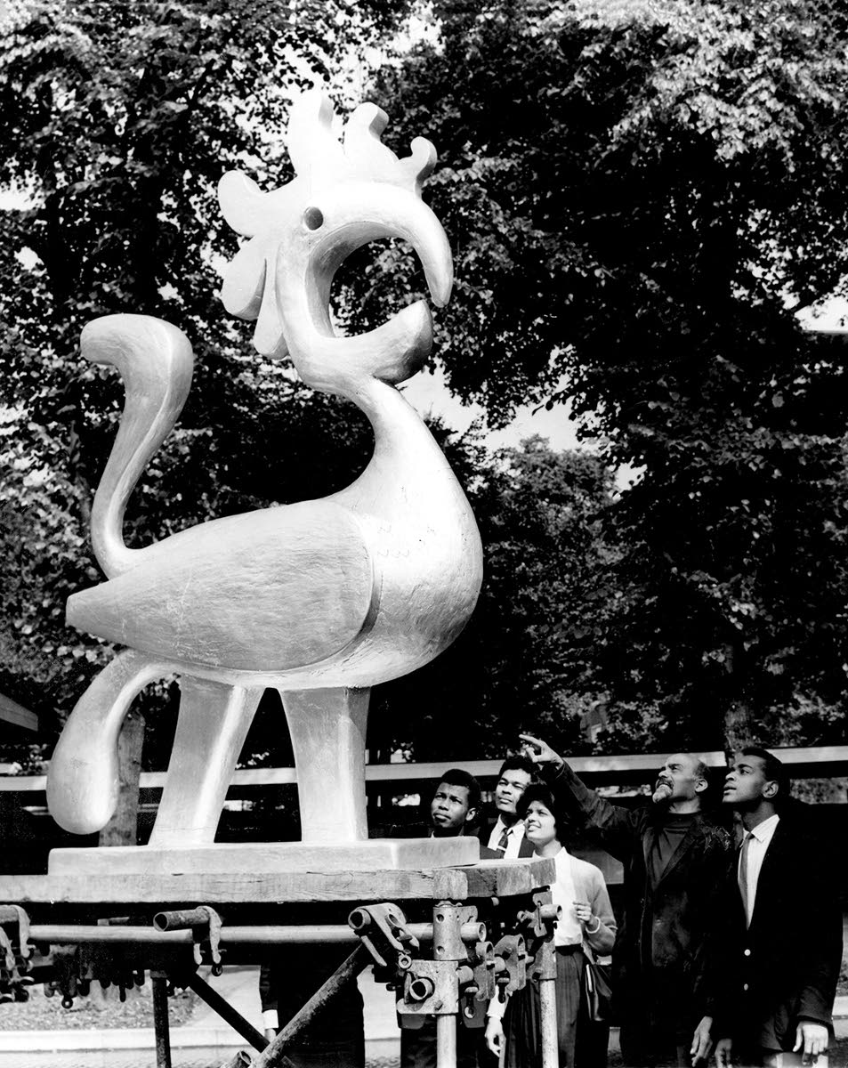 Jamaican sculptor Ronald Moody showing overseas visitors his sculpture of the mythical “Savacou” bird when it was on show on the grounds of the Commonwealth Institute in London.