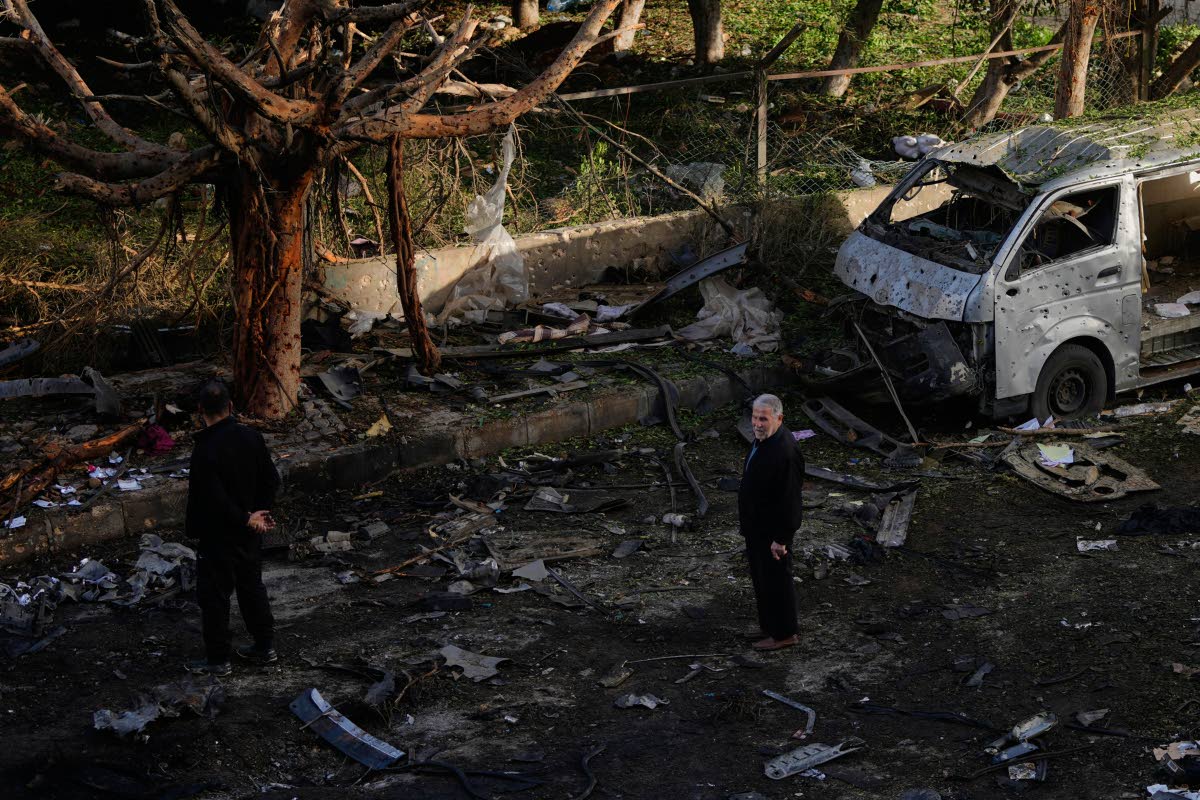 People stand near a damaged van beside scattered debris following an Israeli strike in Beirut, Lebanon.