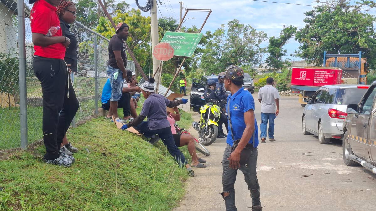 Taxi operators and residents sit along the roadside in Hertford as tensions ease momentarily during the protest calling for urgent road repairs.