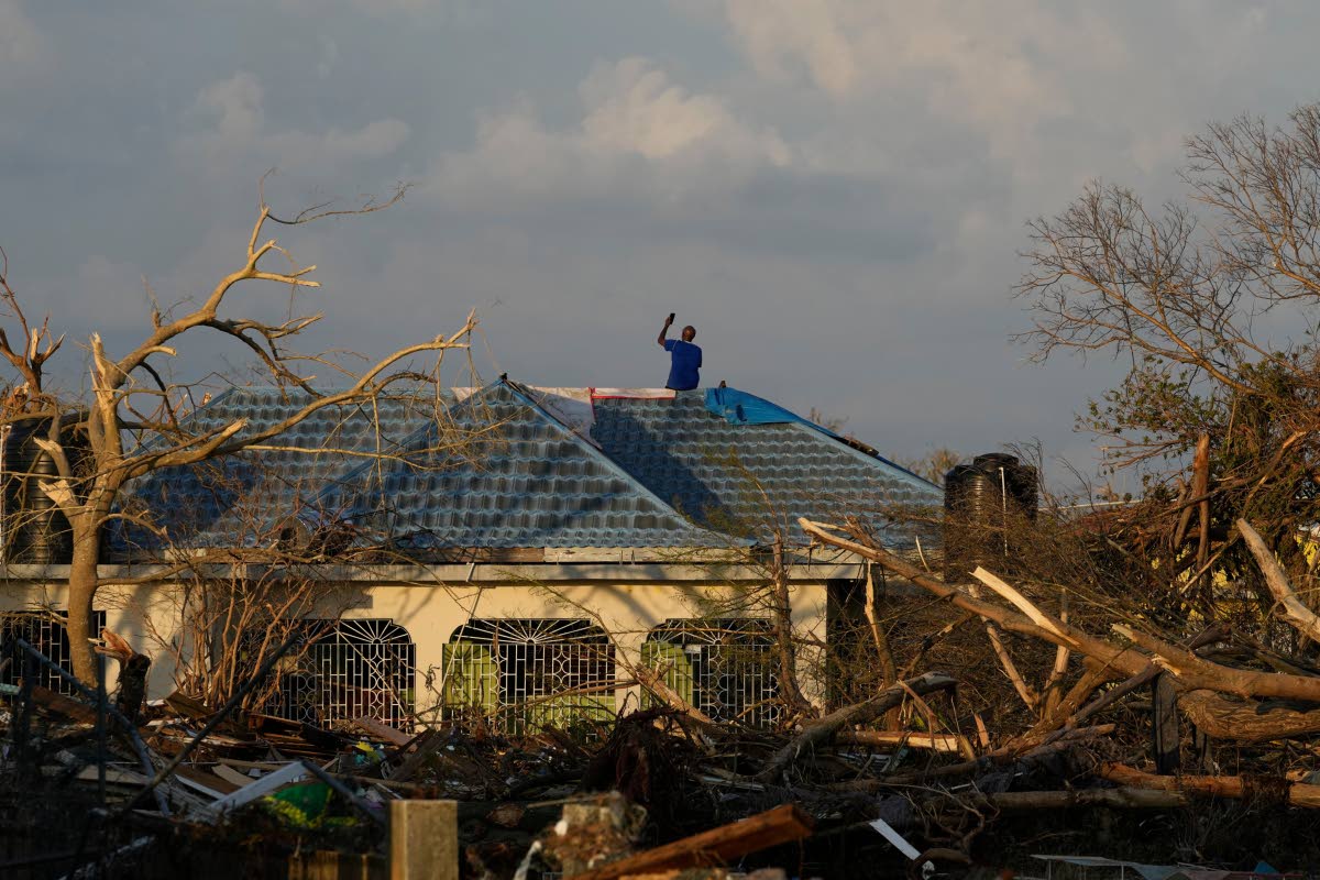 A man searches for cell signal from the roof of his house flooded and damaged by Hurricane Melissa in Black River, Jamaica, Thursday, Oct. 30, 2025. 