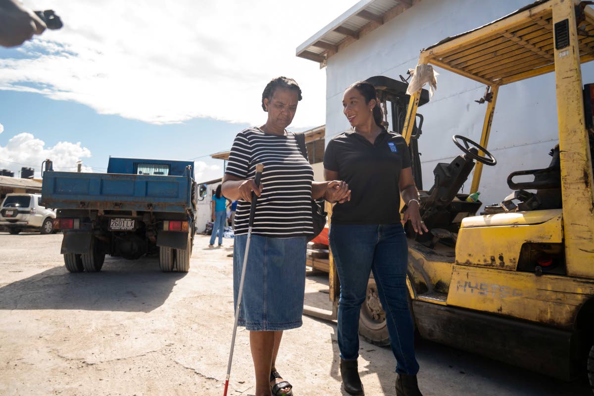 UNDP Assistant Resident Representative Lesley Ann Ennevor (right) supports Villette Neil, a poultry farmer who is blind, in receiving her gift of inputs to recover her poultry business resiliently. 