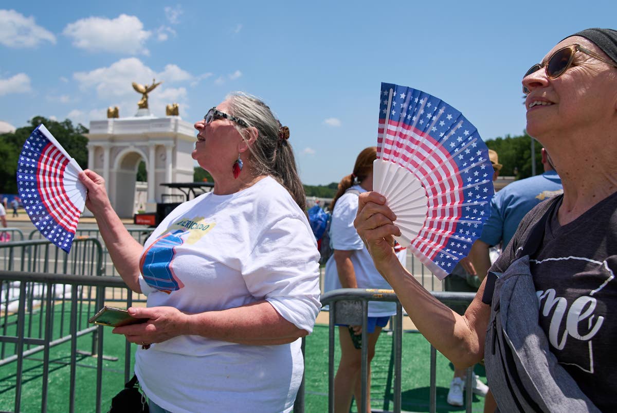 Two women fan themselves while waiting in line for the Ferris wheel at the Great American State Fair on the National Mall, July 1 in Washington.