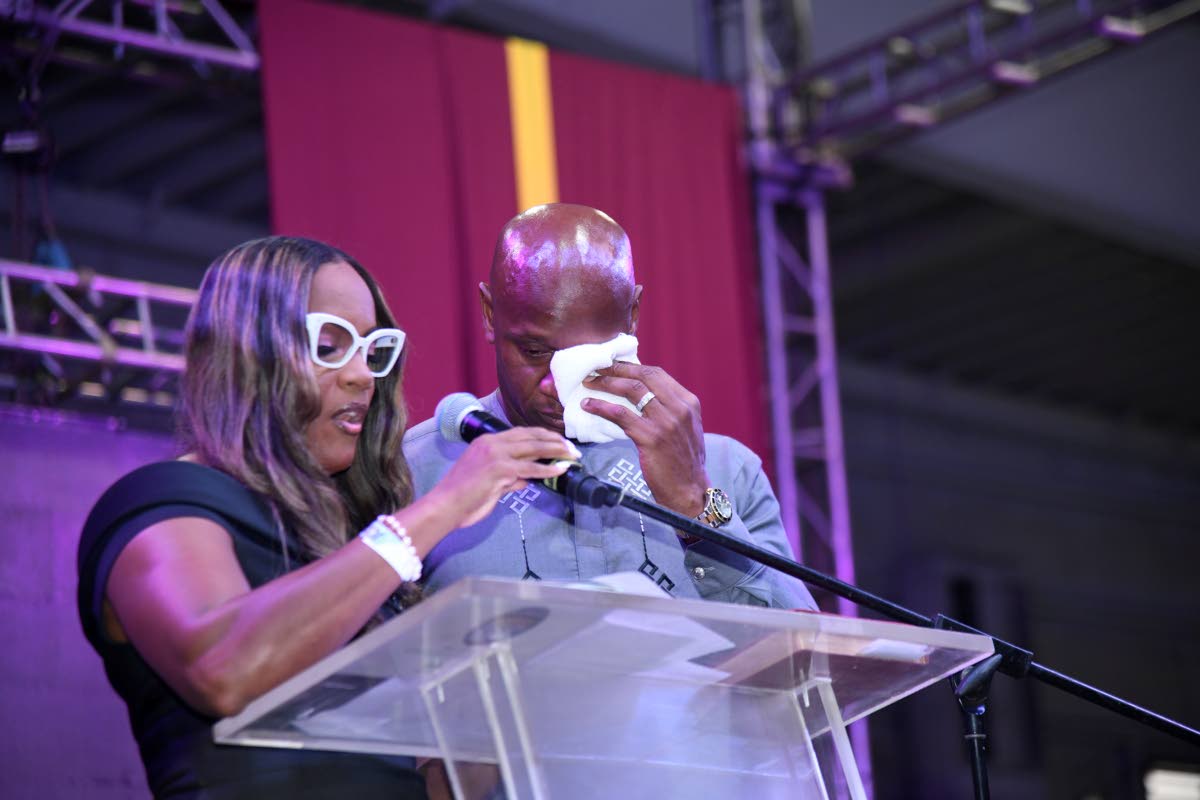 Brigitte Foster-Hylton (left) completes a speech for the visibly distraught Asafa Powell during the service of thanksgiving for the life of his coach, Stephen Francis, at the National Indoor Sports Centre yesterday.  