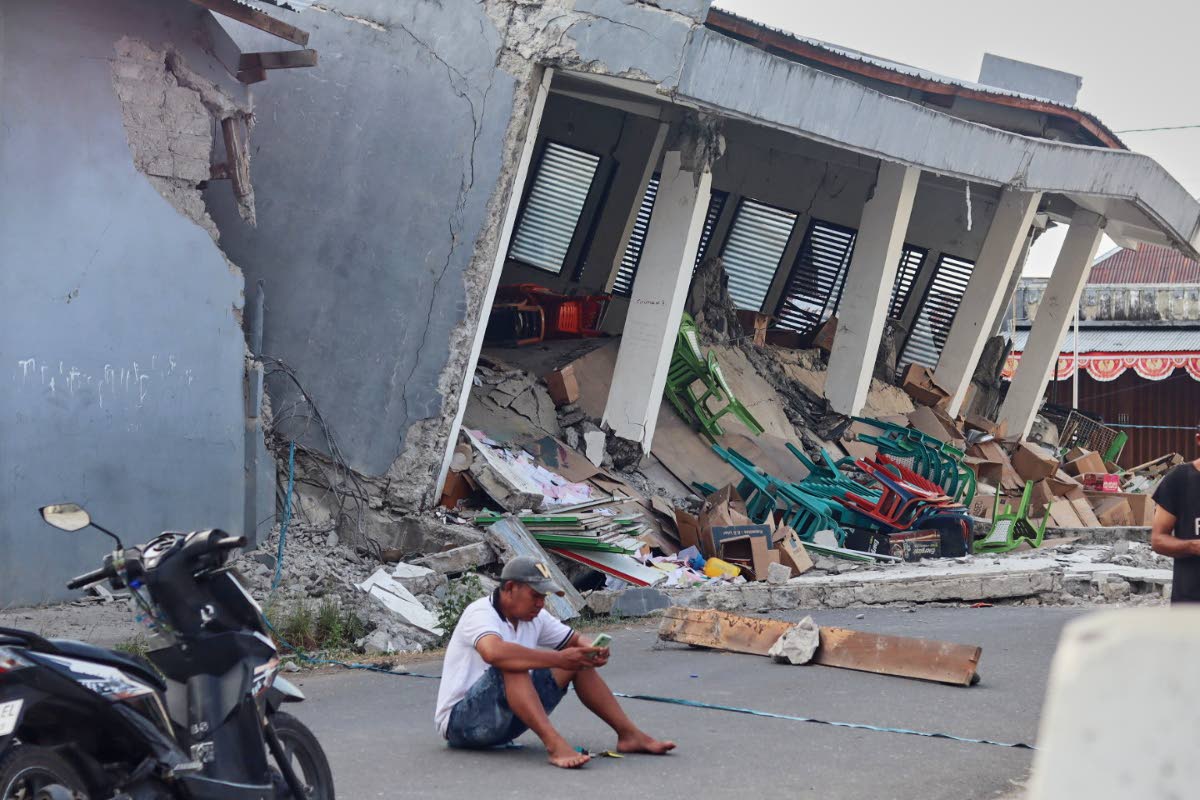 A man checks his phone near a building collapsed due to an earthquake, in Reok, East Nusa Tenggara province, Indonesia, Sunday, Aug. 16, 2026. (AP Photo/Aquila Handayani Abbas)