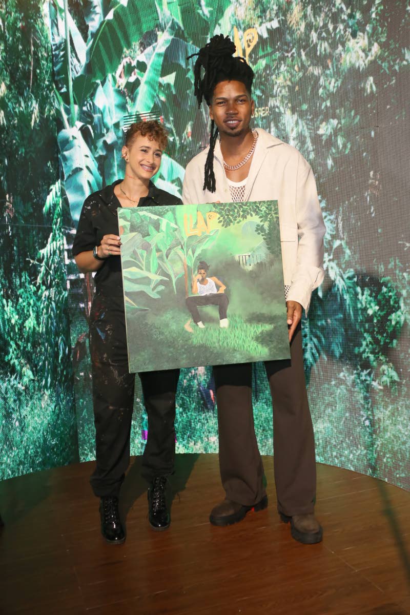Artist Simone Raquel (left) and D’Yani pose for the camera, as he proudly showcases the finished artwork of his album cover, done at the launch. 