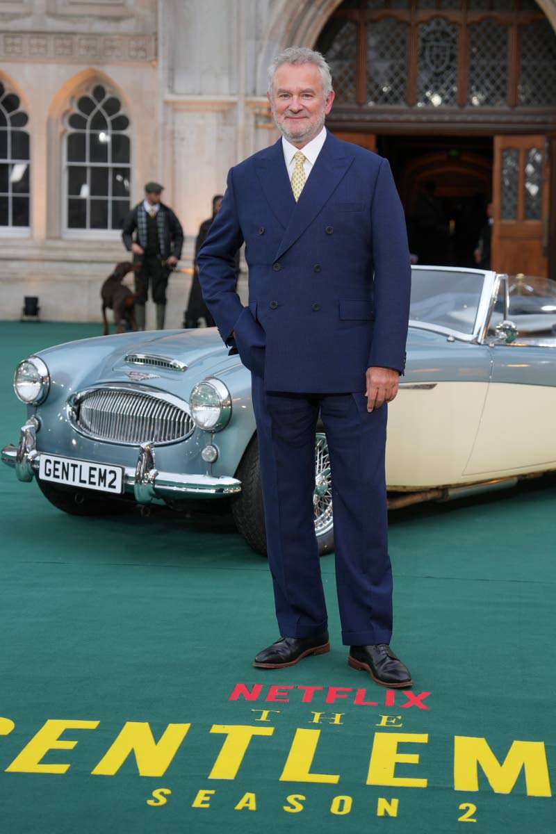 Hugh Bonneville brightens classic navy tailoring with a yellow tie.