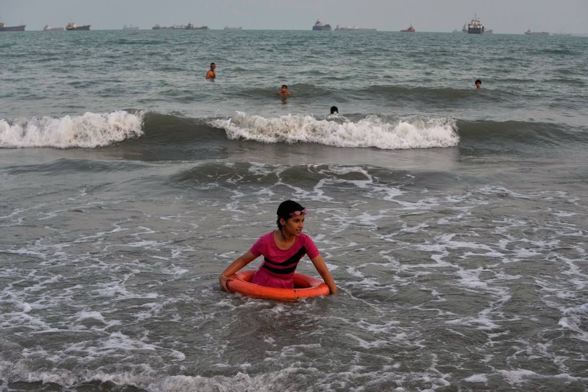 A girl plays in the water with a swim ring as commercial vessels lie anchored in the Strait of Hormuz off Bandar Abbas, Iran.