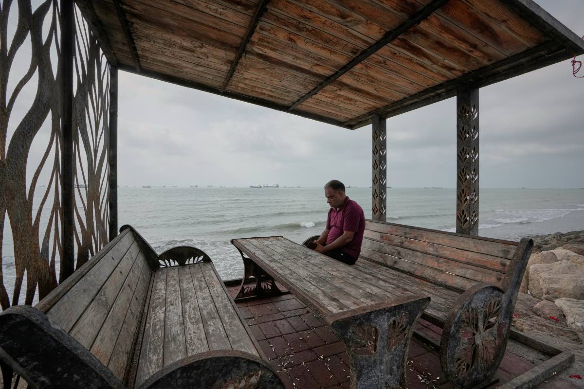 A man rests at a waterfront shelter as commercial vessels lie anchored in the Strait of Hormuz off Bandar Abbas, Iran.