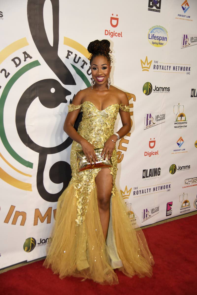 Brithney Clarke, marketing business lead and public relations manager at Digicel, makes a statement in a glittering gold off-the-shoulder evening gown featuring a dramatic front slit and delicate lace appliqués.