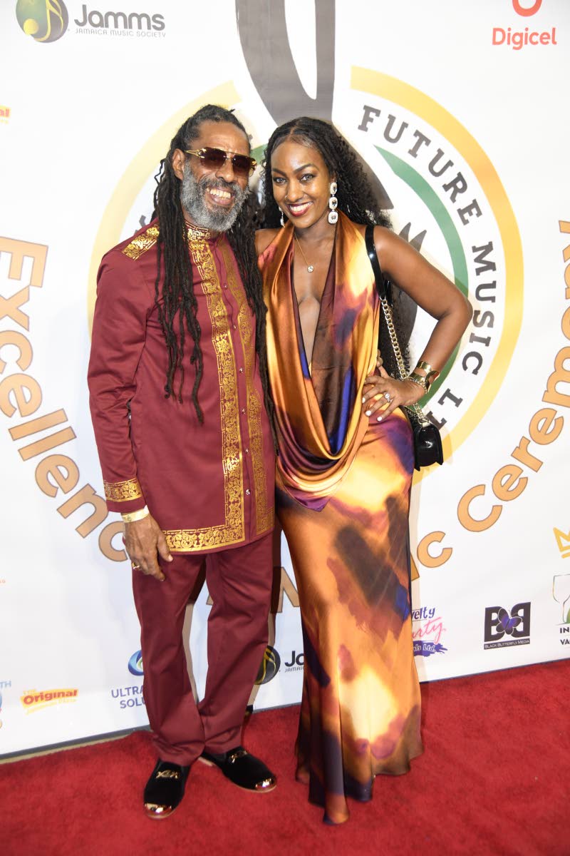 Entertainer Brian Gold wears a maroon and gold-trimmed kaftan suit as he poses with Rochelle Smith, who dons a plunging patterned gown.