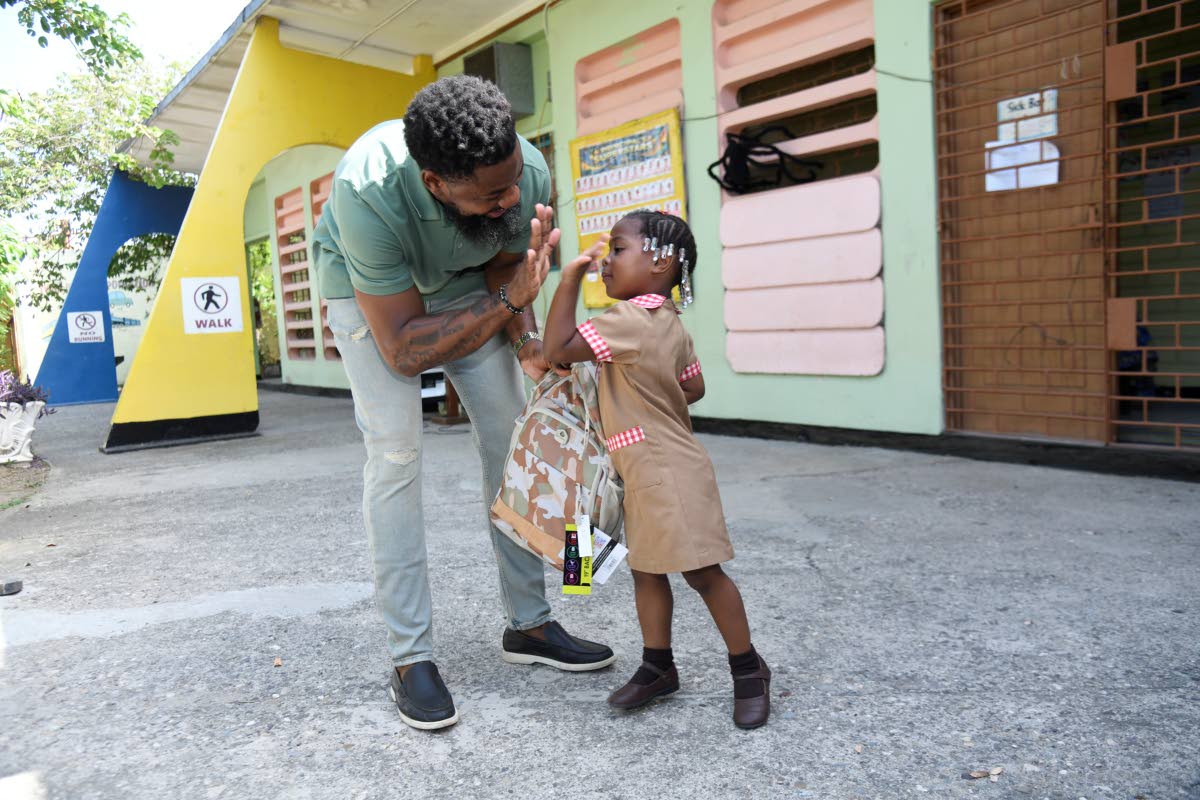 Businessman Oneil ‘Brisco’ Brissett gets a high-five from Mylah Haughton, one of six students who benefited from his back-to-school giveback at Waterford Infant School on Monday.