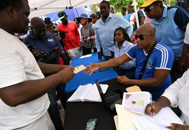 Minister without Portfolio in the Ministry of Economic Growth and Infrastructure Development with responsibility for Land Titling and Settlements, Robert Montague (centre, standing), looks on as Coopers Pen resident, Shawn Ricketts (left), collects his rel
