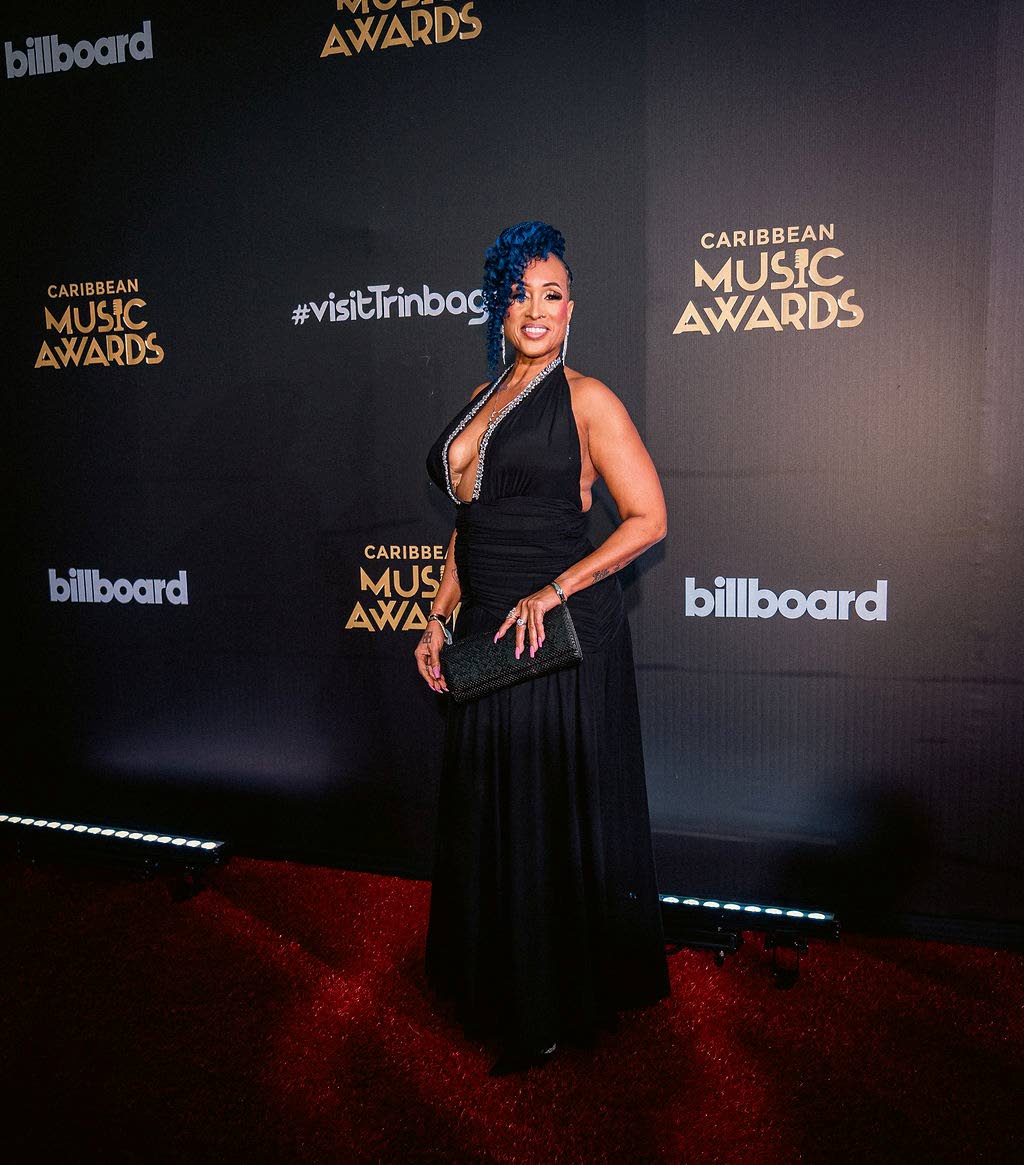 Soca Queen Alison Hinds dons a plunging black gown and matching clutch, complemented by blue tresses styled in an updo.