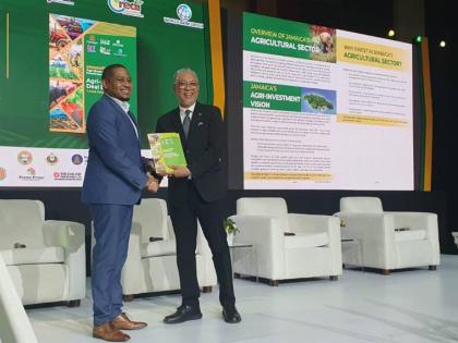Floyd Green, minister of agriculture, fisheries and mining, receives a copy of the agriculture sector investment deal book from Vivion Scully, chief executive officer of the Agro-Investment Corporation, aimed at attracting Investors. 