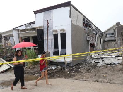 Two women walk past a damaged house after a strong earthquake in Davao City, southern Philippines on Friday October 10, 2025. (AP Photo/Manman Dejeto)