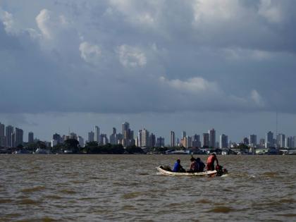 A boat sails on the bay of the Guama River with Belém, Brazil, in the background.					      
