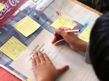 A Grade 2 student of Shichigo Elementary School, Sendai, completes a form on disaster preparedness. On the desk is a poster of the route they take to get home. On the Stick-it notes are the suggestions given by students.