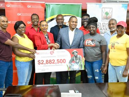Minister of Agriculture, Fisheries and Mining, Floyd Green (third right, front row), shakes hands with the GraceKennedy (GK) Group’s Head of General Insurance, Tammara Glaves-Hucey, during the symbolic handover of a $2.88 million insurance payout to 98 R