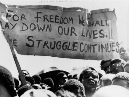 A banner is held aloft above black students in Johannesburg, South Africa, in the township of Soweto where they rallied after the funeral of a 16-year-old black student who died in jail on October 18, 1976. 