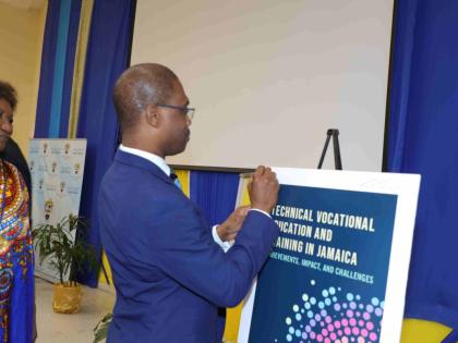 Dr Kevin Brown, president of the University of Technology, Jamaica and chairman of UTech Press, signs a replica of the cover of Technical Vocational Education and Training in Jamaica: Achievements, Impact, and Challenges, launched on November 26.