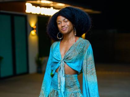 Web Designer, Samiyyah Andrewin-Miranda, stuns in a flowing turquoise outfit featuring a tie-front top with billowy sleeves and a smocked waist, paired with a tiered skirt that adds movement to the look.