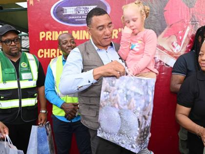 Prime Minister, Dr Andrew Holness, gives a gift to a child during a Christmas treat held at the Petersfield High School in Westmoreland on December 13. Also present was Minister of Labour and Social Security, Pearnel Charles Jr. (background, second left).