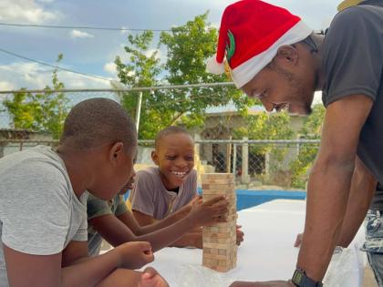 Devon Dallas, of  A-List Marketing and Entertainment Group, engages children in a lively game of Jenga during the ‘Joy to the West’ initiative in Westmoreland. The event brought festive fun and support to families impacted by Hurricane Melissa.