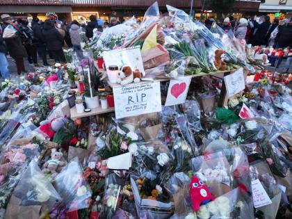 People stand around floral tributes and candles placed outside the sealed off Le Constellation bar in Crans-Montana, Swiss Alps, Switzerland on January. 3, 2026, where a devastating fire left dead and injured during the New Year's celebrations. 