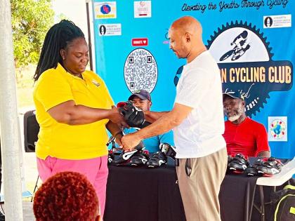 Elevation Cycling Club secretary Taneish Dixon (left) makes a symbolic presentation to Kevin Dillon of Dillies Cycle World during the ceremony at which 80 pairs of high-performance cycling shoes, valued at more than US$8,000, were donated to key cycling in