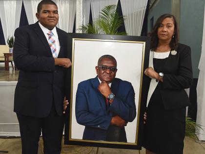 Daniel Smith, son of Anthony Smith, and his mother, Karen Smith, hold a photograph of Anthony Smith, former CEO of the RJRGLEANER Communications Group, during a thanksgiving service for his life held yesterday inside the Karl Hendrickson Auditorium at Jama