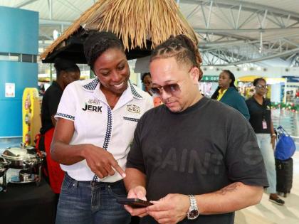 Sabrina Watson (left), global category manager – seasonings, sauces and spices at Grace Foods, guides traveller Richard Ho-sing in navigating the donation site at the Norman Manley International Airport during the Bring Jamaica Home activation.