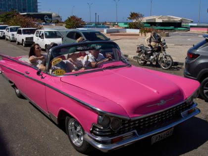 Tourists travel in a classic American car next to a line of drivers waiting to buy fuel for their cars in Havana, Cuba, on February 16, 2026. 